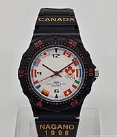 Front view of McDonalds Nagano 1998 Olympic collectible watch, showing white dial with country flags, McDonalds logo, and Olympic rings. Black strap with gold 'CANADA' and 'NAGANO 1998'.