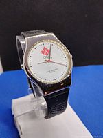 Front view of McDonalds Nagano 1998 Olympic collectible watch face showing white dial with red maple leaf and Olympic rings logo, gold bezel, and black strap.