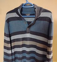 Front view of the striped men's sweater hanging on a hanger showing knit pattern, colors, and button-up collar detail.