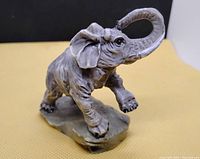 Grey elephant figurine on a textured base, showing front-right side profile.