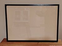 Front view of the black wood picture frame with glass, showing the empty frame standing upright against a white wall.