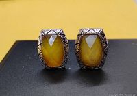 Front view of two silver-toned vintage earrings with yellow faceted stones showing faceted surface and geometric border pattern.