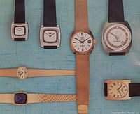 Photo showing seven Longines vintage watches with different case shapes and bands on blue fabric background.
