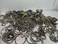 Wide view of large mixed assortment of silver-tone costume jewelry including bracelets, bangles, and charm bracelets with colorful beads and rhinestones.