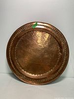 Front view of the round copper tray showcasing the hammered texture and beaded decorative edge.