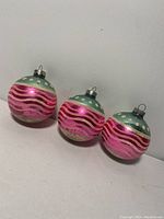 Three antique glass spherical Christmas ornaments with baby blue tops and pink bodies with wave and dot patterns