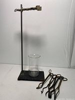 Photo showing the metal test tube stand with a clear glass Pyrex beaker and several metal clamps arranged beside it.