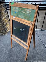 Full view of antique school chalk sign with wood frame standing, showing top green panel with alphabet and numbers and lower chalkboard.