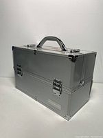 Photo showing overall front side of silver aluminum makeup case with handle and latches, showing minor scratches.