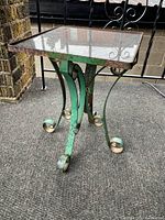 Photo showing whole table with green painted metal base and smoked glass top on outdoor carpeted balcony.