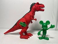 Green Mickey Mouse figurine and red dinosaur toy side view showing size and details