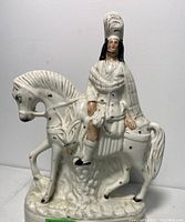 Front view of white glazed Staffordshire porcelain figurine showing Scottish hunter with feathered hat on horse, with visible brown spots and hand-painted details