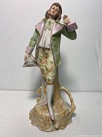 Front view of bisque figurine showing from the base to the head with detailed pastel color clothing and textured floral base.