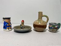 Front view of the four items on white background showing varying sizes and details of each miniature jug and gnome figurine