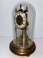 Full view of the German mantel clock encased in a glass dome showing its brass base and ornamental details.