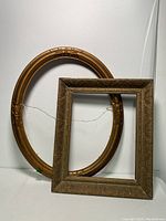 Two vintage picture frames: one oval and one rectangular, both gold-toned and decorative, displayed against a white background.