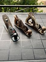 Three vintage hand planes arranged in a row, showing all planes with their wooden or plastic handles and metal bodies on a table surface outdoors, illustrating the lot's composition.