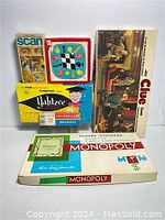 Photo shows a collection of vintage board games including Monopoly, Clue, Yahtzee, Cribbage, Scan matching game stacked together on a white surface.