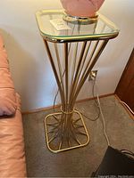 Full view of brass pedestal table with square glass top beside a sofa.
