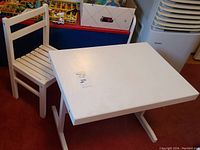 White wooden child's desk and chair set positioned on red carpet with visible scratches and use marks on surfaces.