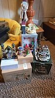 Multiple holiday village pieces arranged on boxes including lit buildings, a carousel, and nutcracker figures.