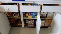 Kitchen cabinet drawers open showing storage bags, kitchen tins, and other containers inside.