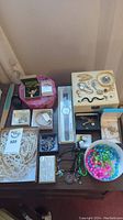 Entire assortment of costume jewelry including boxed items, loose necklaces, bracelets, brooches, and beads on table