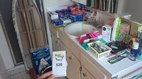 Photo showing a bathroom countertop with sink and a variety of personal care, first aid supplies, tissues, and other bathroom items arranged on the countertop.