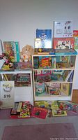 Photo of two white shelving units holding children's books and boxed games, with some books and games on floor in front