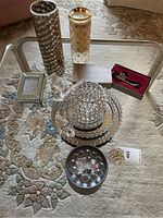 Full view of various mirrored trays, crystal ball candle holders, decorative small box and key pendant on glass table