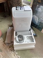 Portable AC unit on carpet with styrofoam packaging showing exhaust hose and vent adapters