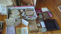 Photo showing assorted photo frames in boxes and spread out on floor, including gold oval and rectangular frames, dark wood frame, and others.