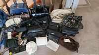 Wide view showing 22 purses of multiple colors and styles arranged on floor including black, brown, leopard print, and beige bags