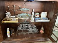 Wide view of bottom shelf showing various royal commemorative items including Wedgwood plates, barware glass set, bells, and decorative pieces.