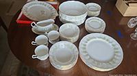 Photo showing assorted plates, teacups, saucers, gravy boat and bowls arranged on a table with a floral patterned rim in green and gold.
