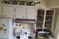 Kitchen stove area with white refrigerator, white toaster, black toaster oven, and cabinet with kitchen essentials