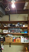 View of workshop shelving with various small drawers, boxes, and baskets containing hardware and tools under a light bulb.