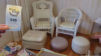 Wide shot showing two white wicker chairs with floral cushions and three small round ottomans in beige, gray and white.
