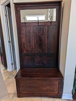 Full frontal view of the wooden hall tree showing three black metal hooks on the back panel and the bench below.