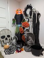 Photo shows the full assortment of Halloween decorations including inflatable pumpkin man, wooden skull wall hanging, resin gargoyle and dragon statues, plastic cauldrons, jack-o-lantern items, and a dark wreath.