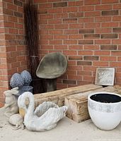 Overview of lot showing concrete chair, timber beams, swan statue, rabbit statue, plant pot with soil, plaster plaque, cone statues, and bundle of sticks.