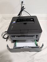 Brother HL-L2320D monochrome laser printer with paper tray open and power cable attached