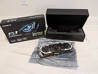 Gigabyte Nvidia GeForce GTX 980 Ti graphics card displayed on anti-static bag with original box and black protective storage box in background.