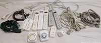 Photo showing The Clapper power switch, several power bars, multiple extension cords, power timers and night light arranged on white surface