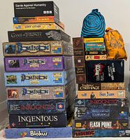 Stacked box spines showing Cards Against Humanity, Jambo, Lost Cities, Game of Thrones, Dominion series, Inkognito, Ingenious, Blokus, Time's Up, Can't Stop, Lovecraft Letter, Landlord!, Mille Bornes, Coloretto, Diabolo, Bang!, Petits Meurtres, Traders of Carthage, San Juan, Race for the Galaxy, Flash Point, Pandemic
