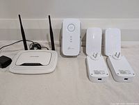 Full group shot showing one TP-LINK router, one range extender, and four powerline ethernet extenders on carpeted floor.