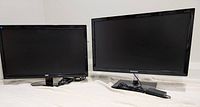 Two monitors side by side on a blanket, AOC on left, Samsung on right, both monitors powered off, stands and power cords visible.