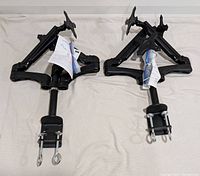 Two black Mount-It! MI-763 triple monitor mounts laid side by side showing mounting clamps and bottom view.
