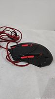 Side angle photo of black and red gaming mouse with braided cable on white surface.
