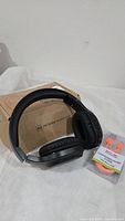 Black over-ear FM radio headphones with original cardboard box and a pack of foam earplugs beside them.